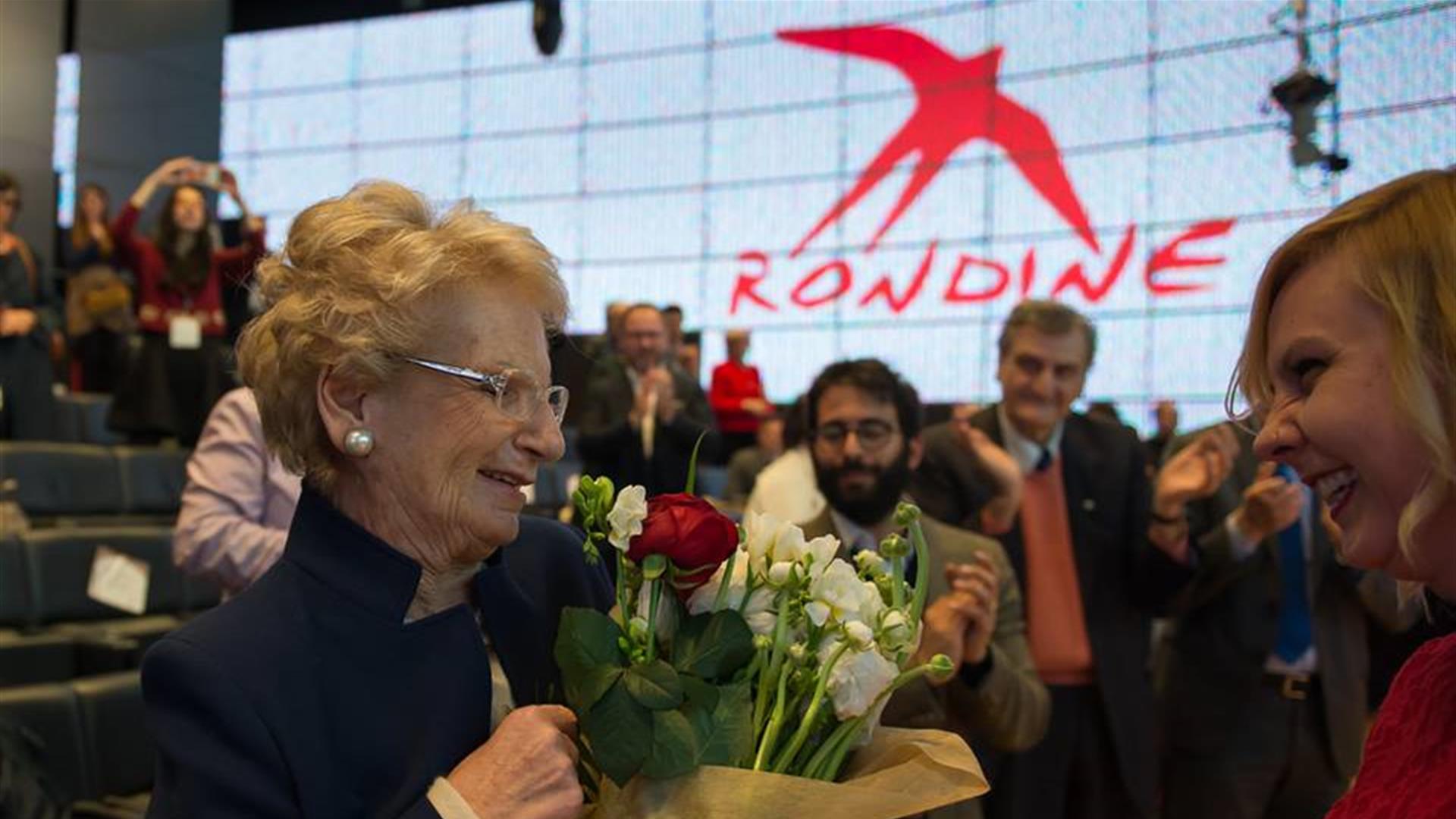 Liliana Segre con logo Rondine rosso sullo sfondo e mazzo di rose